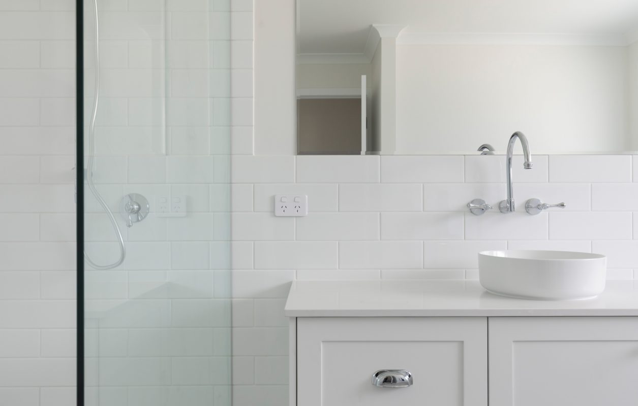 Close up of white bathroom with large mirror, white tiles, white basin cabinet, and glass shower-screens