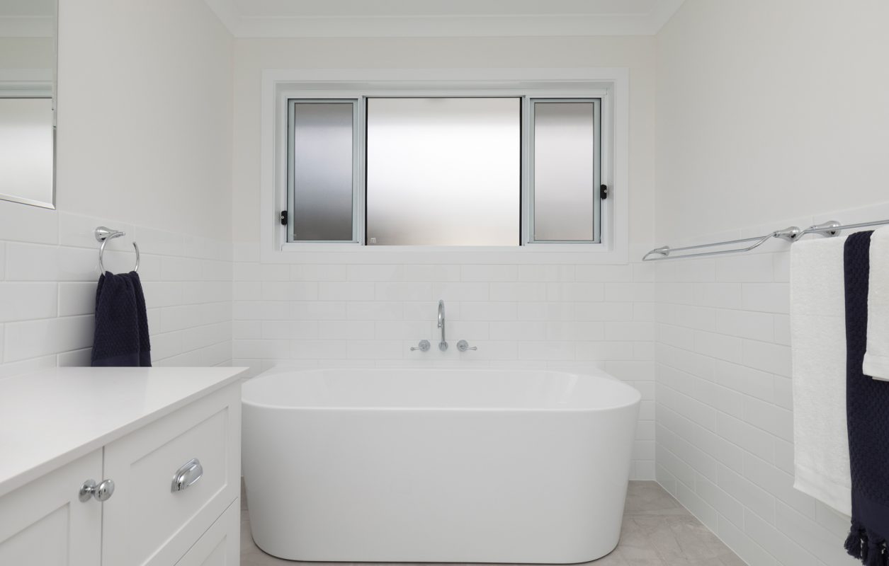 White bathroom with deep soaking tub, high windows, white sink cabinets, and towels hanging on the side