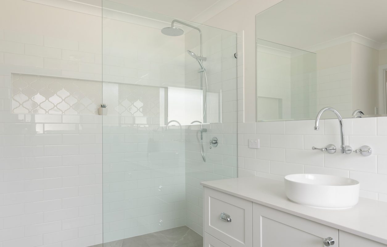 White bathroom with big mirror, white tiles, glass shower-screens, and a small indoor plant