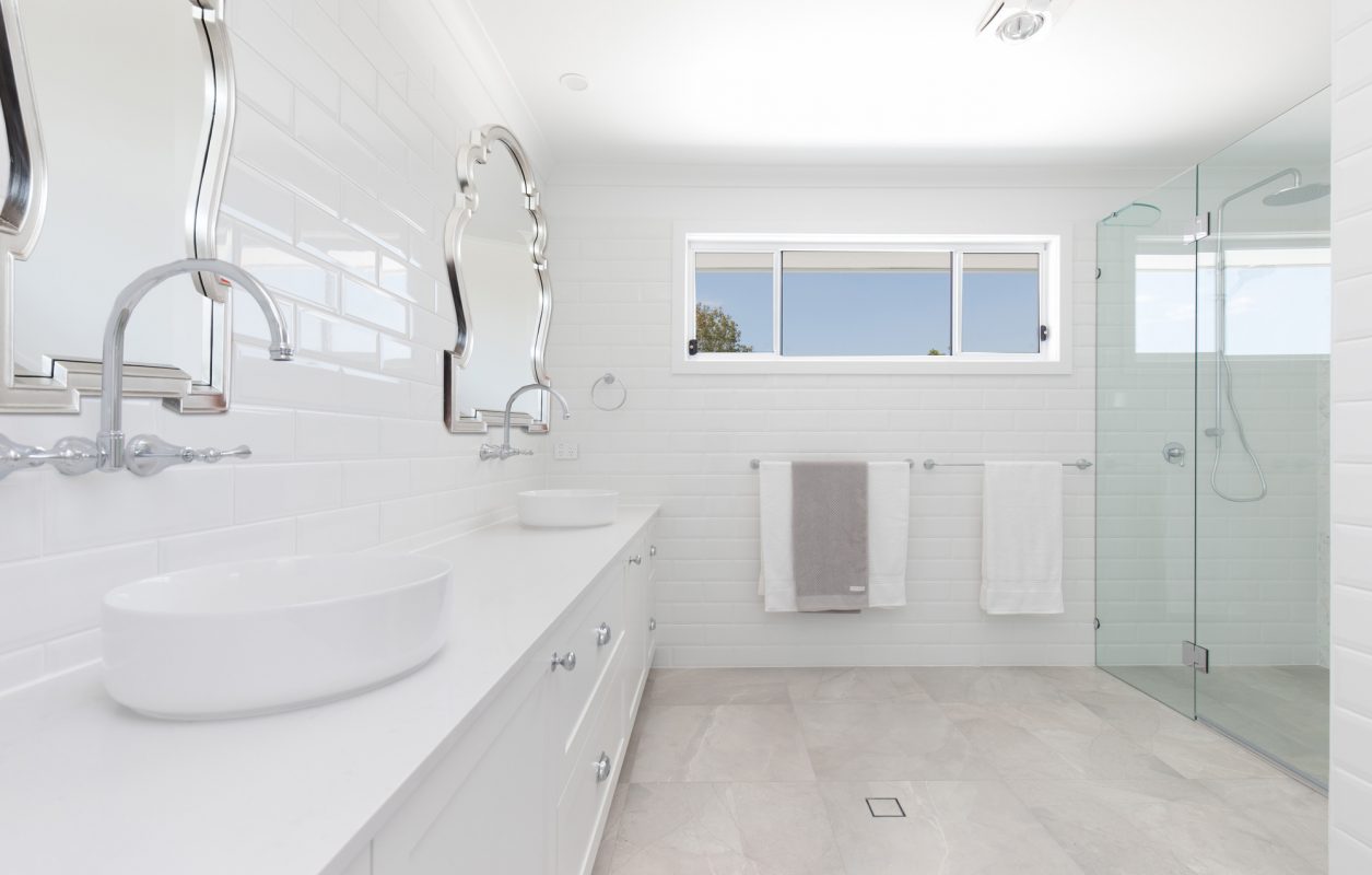 Light and bright bathroom with white basin, silver moorish mirrors, glass shower-screens, high window, white walls and tiles