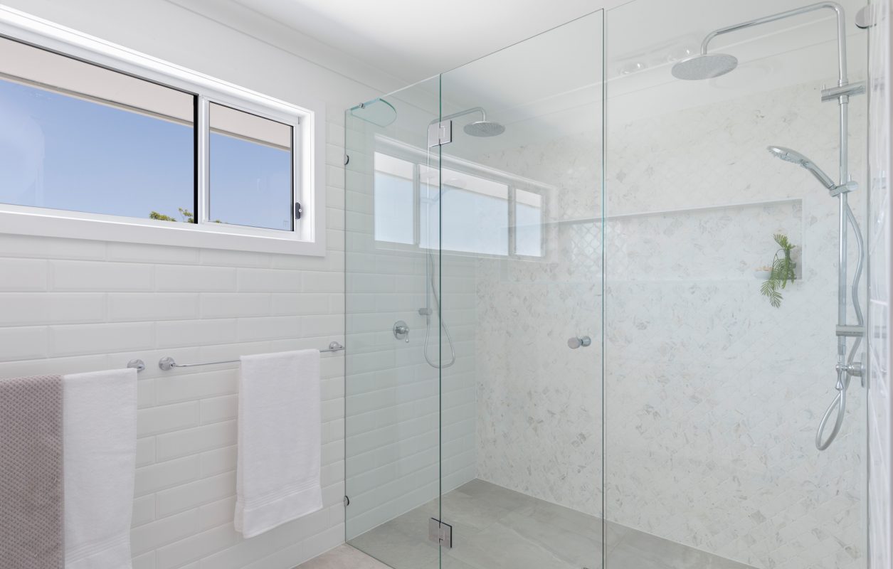 Light and bright bathroom with white tiles, glass shower screens and a high horizontal window