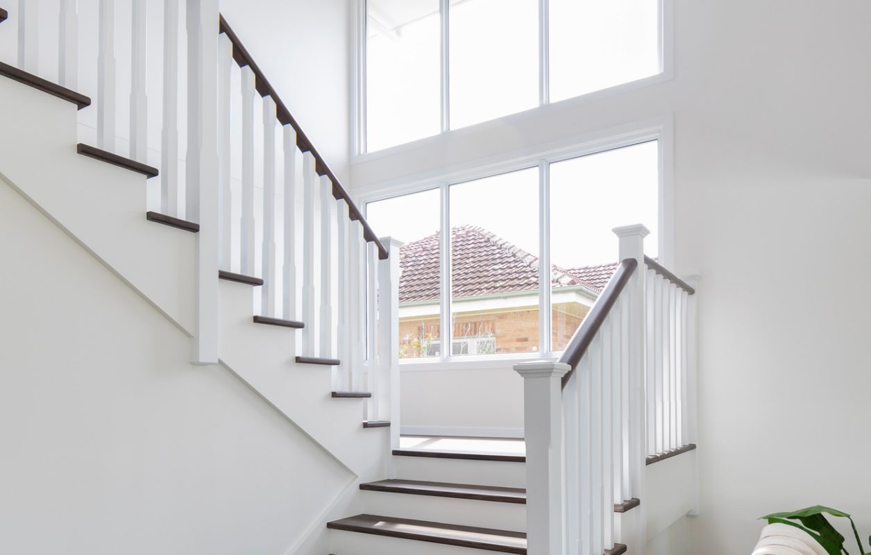Dark brown and white stairs with a large window and a modern chandelier in a white Queenslander and Hampton style house