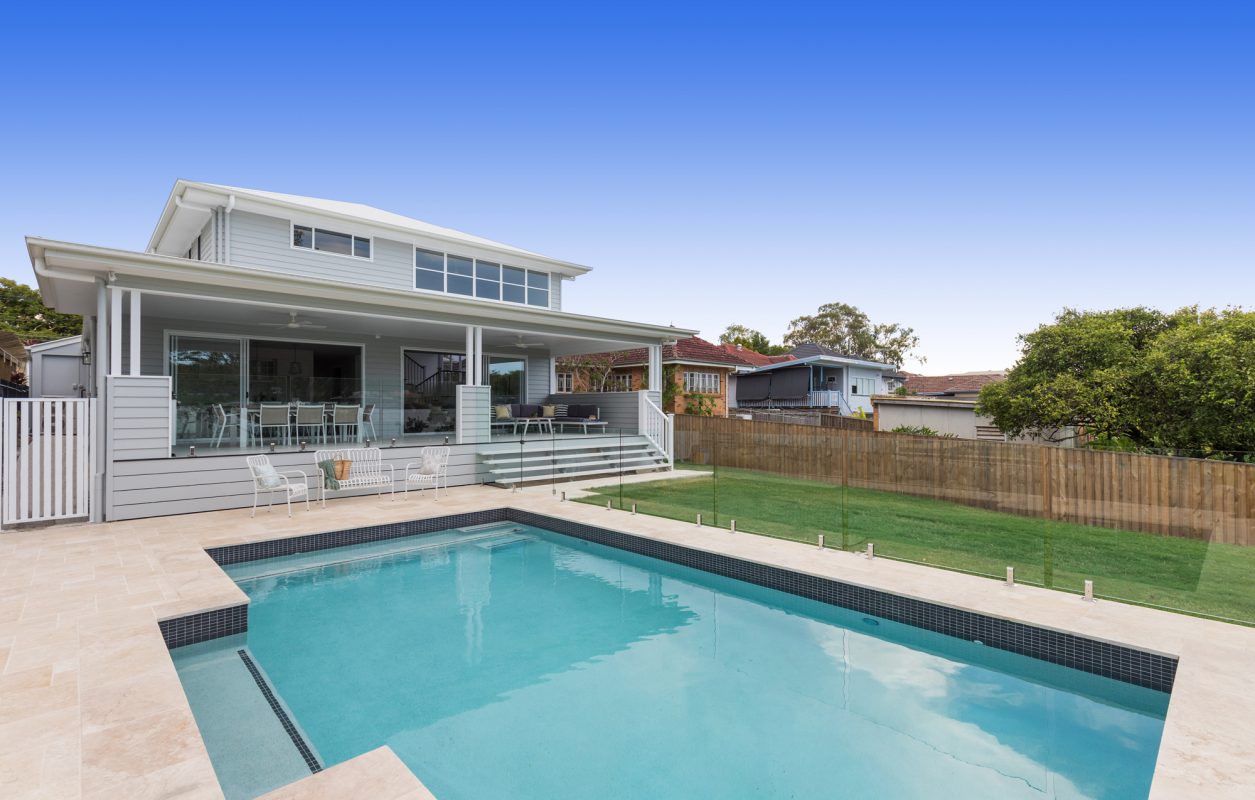 Backyard swimming pool with frameless glass pool fencing in a white Hampton and Queenslander style house