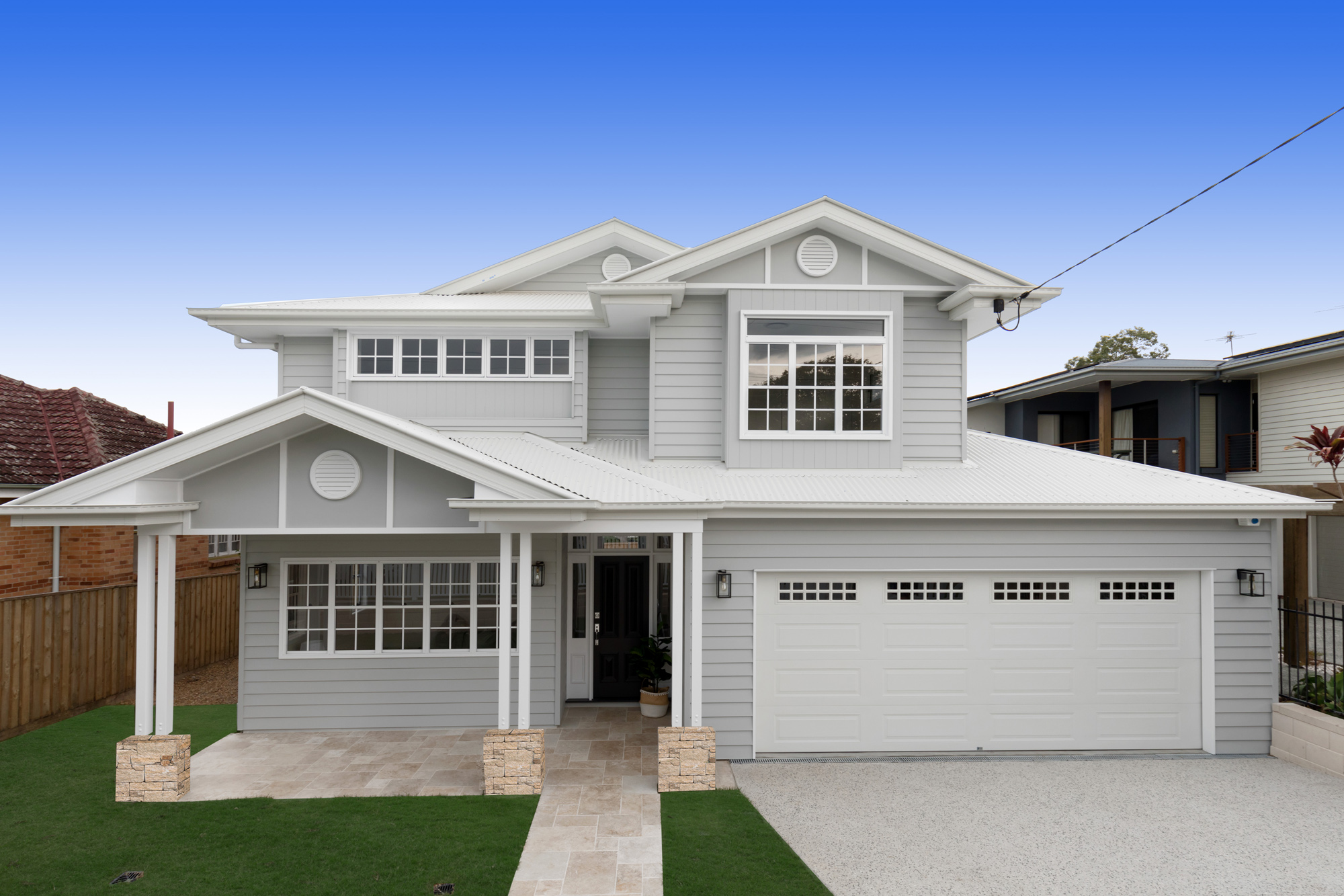 Full frontal view of a white Hampton and Queenslander style house with a garage and travertine pavers in a French-lay pattern